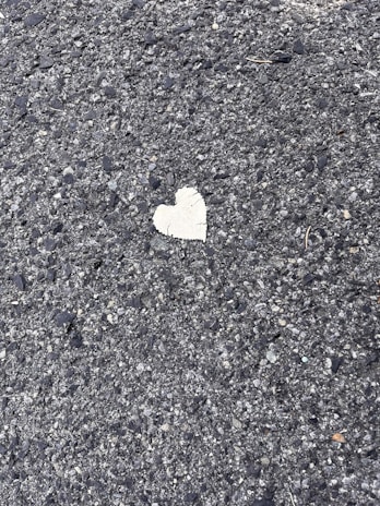 A rough textured asphalt surface with a single, small heart-shaped patch in a contrasting lighter color.