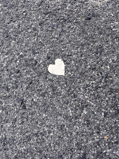 A rough textured asphalt surface with a single, small heart-shaped patch in a contrasting lighter color.