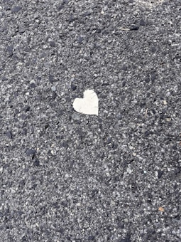 A rough textured asphalt surface with a single, small heart-shaped patch in a contrasting lighter color.