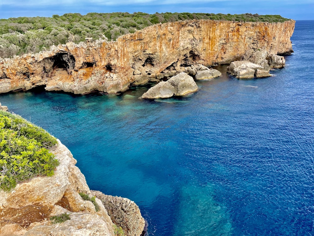 a blue body of water next to a rocky cliff