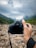 A person's hand holding and focusing a DSLR camera towards a scenic landscape of rocky terrain and distant green hills under a cloudy sky.