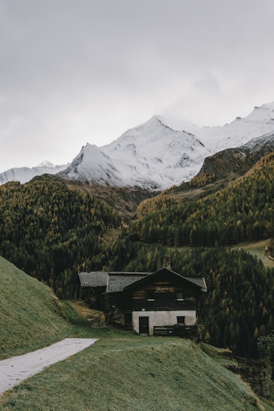 A scenic mountain hut surrounded by lush greenery and stunning peaks.