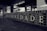 A black and white tiled wall displays large letters spelling out 'FRATERNIDADE,' which means brotherhood in Portuguese. Surrounding the main word are smaller words and years, possibly representing historical events or names. The setting appears to be an underground station or public space with additional artwork visible in the background.