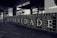 A black and white tiled wall displays large letters spelling out 'FRATERNIDADE,' which means brotherhood in Portuguese. Surrounding the main word are smaller words and years, possibly representing historical events or names. The setting appears to be an underground station or public space with additional artwork visible in the background.