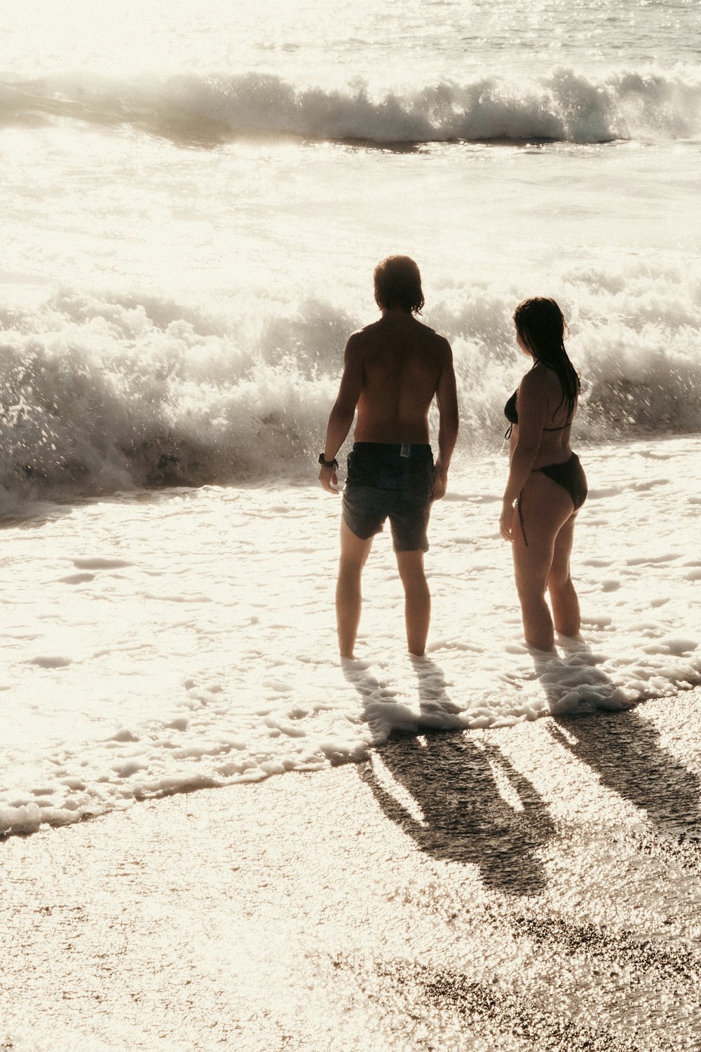 a man and a woman standing on a beach next to the ocean