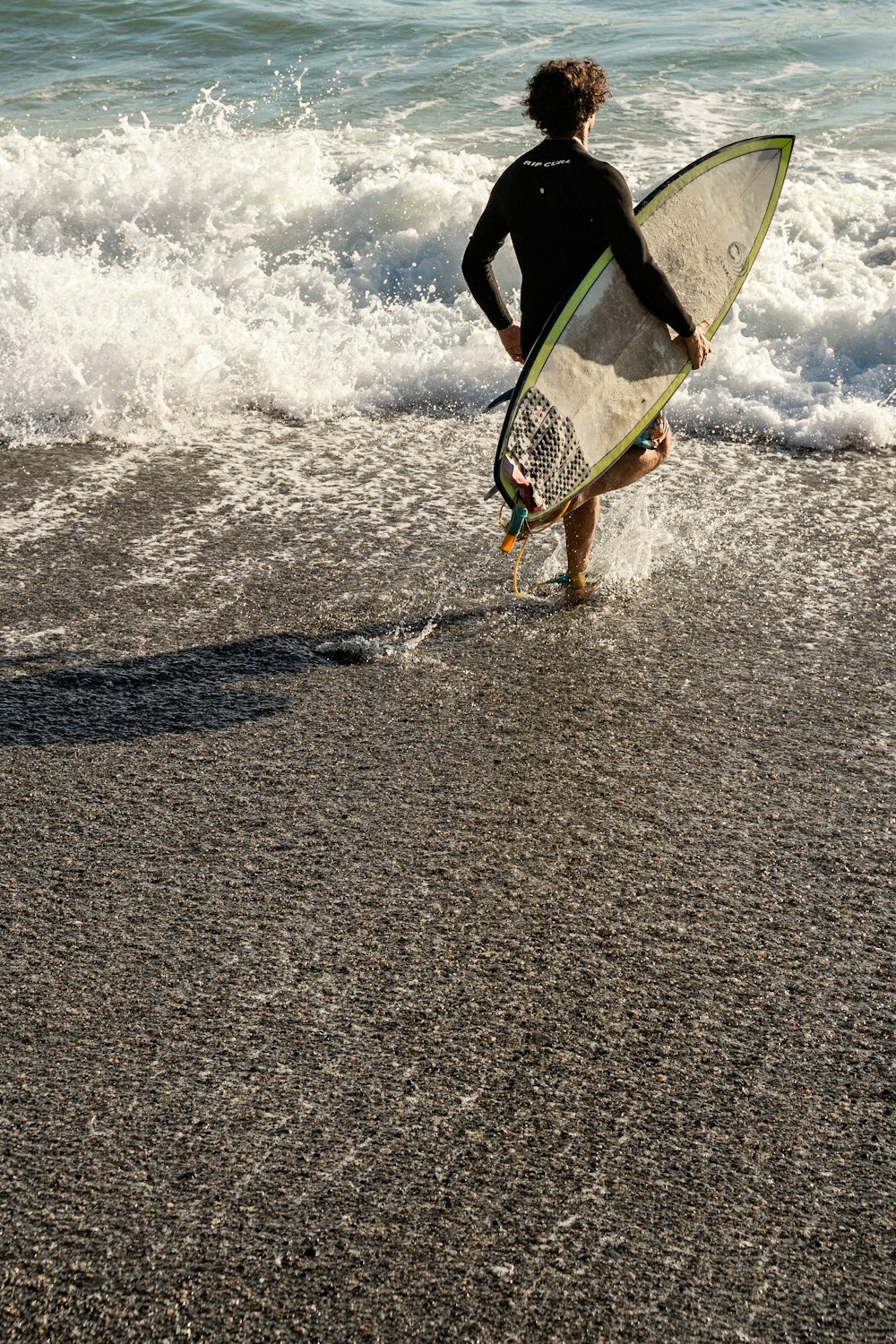 un uomo che tiene in mano una tavola da surf che cammina nell'oceano