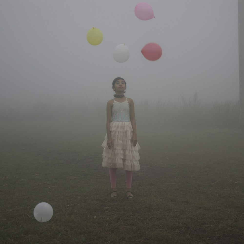 a girl standing in a field with balloons floating in the air
