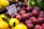 A market display of fresh fruits, including several plums in the foreground, with a price tag showing the cost per kilogram in Euros. There are also some lemons and avocados visible around the plums.