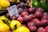 A market display of fresh fruits, including several plums in the foreground, with a price tag showing the cost per kilogram in Euros. There are also some lemons and avocados visible around the plums.