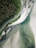A winding road runs parallel to a coastline, bordered on one side by dense green forest and on the other by white sandy beach and clear turquoise water. The area appears serene and untouched, offering a blend of rugged natural beauty and tranquility.