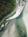 A winding road runs parallel to a coastline, bordered on one side by dense green forest and on the other by white sandy beach and clear turquoise water. The area appears serene and untouched, offering a blend of rugged natural beauty and tranquility.