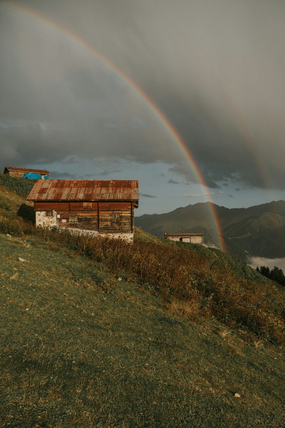 uma casa em uma colina com um arco-íris ao fundo
