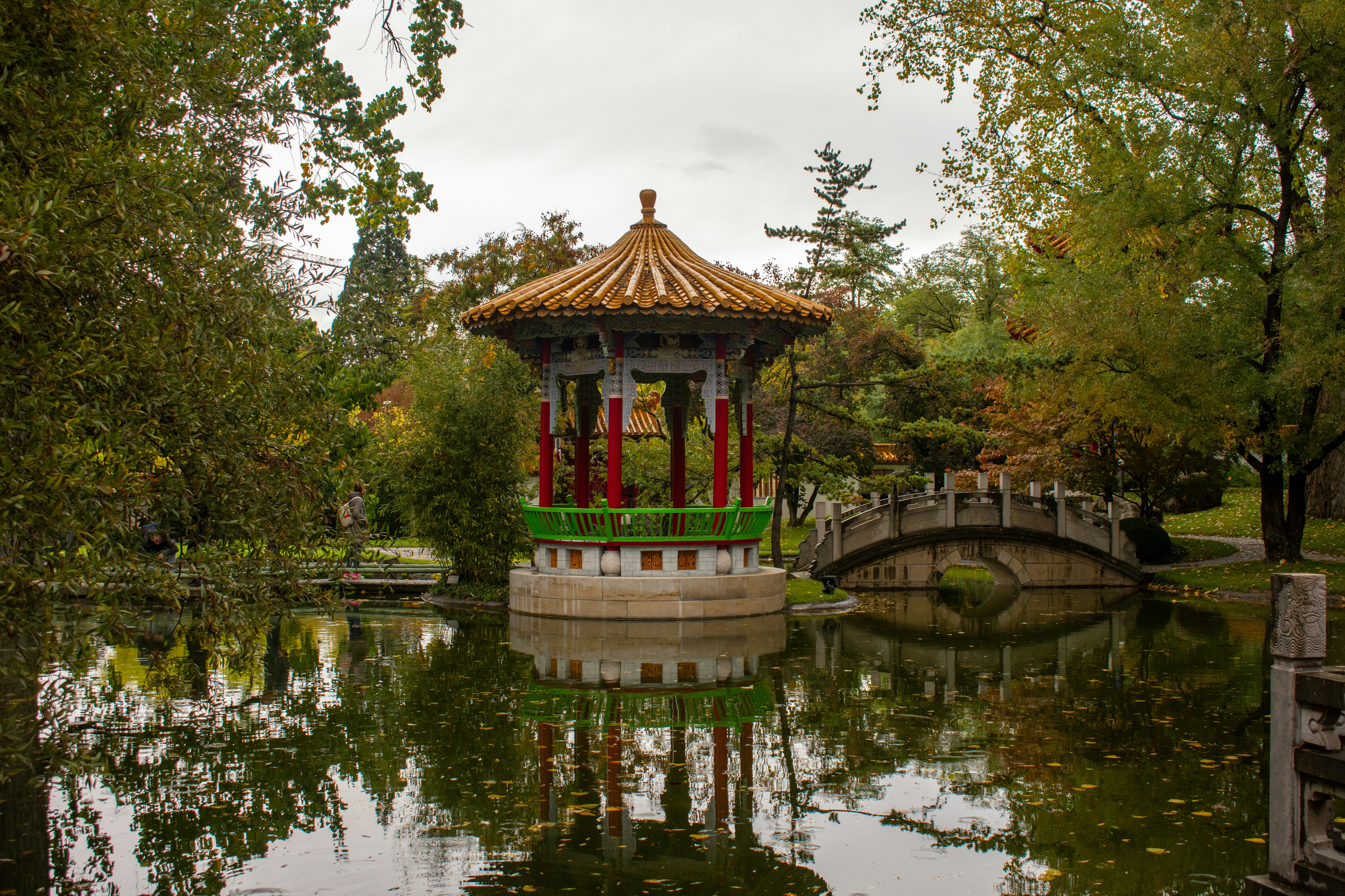 a gazebo in the middle of a pond with a bridge in the background, 