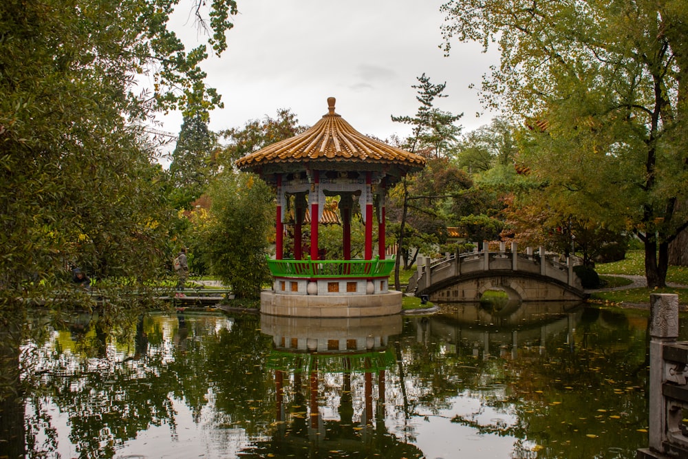 a gazebo in the middle of a pond with a bridge in the background