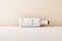 A minimalist, horizontally positioned white matte bottle with a wooden cap design. Large black letters 'BTL' are prominently displayed on the side. The background features a gradient of beige to cream, creating a clean, modern aesthetic.