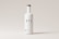 A tall white bottle with a minimalistic design is centered against a light gray background. The bottle features bold black letters spelling 'BTL' and additional smaller text below. It has a round wooden cap.