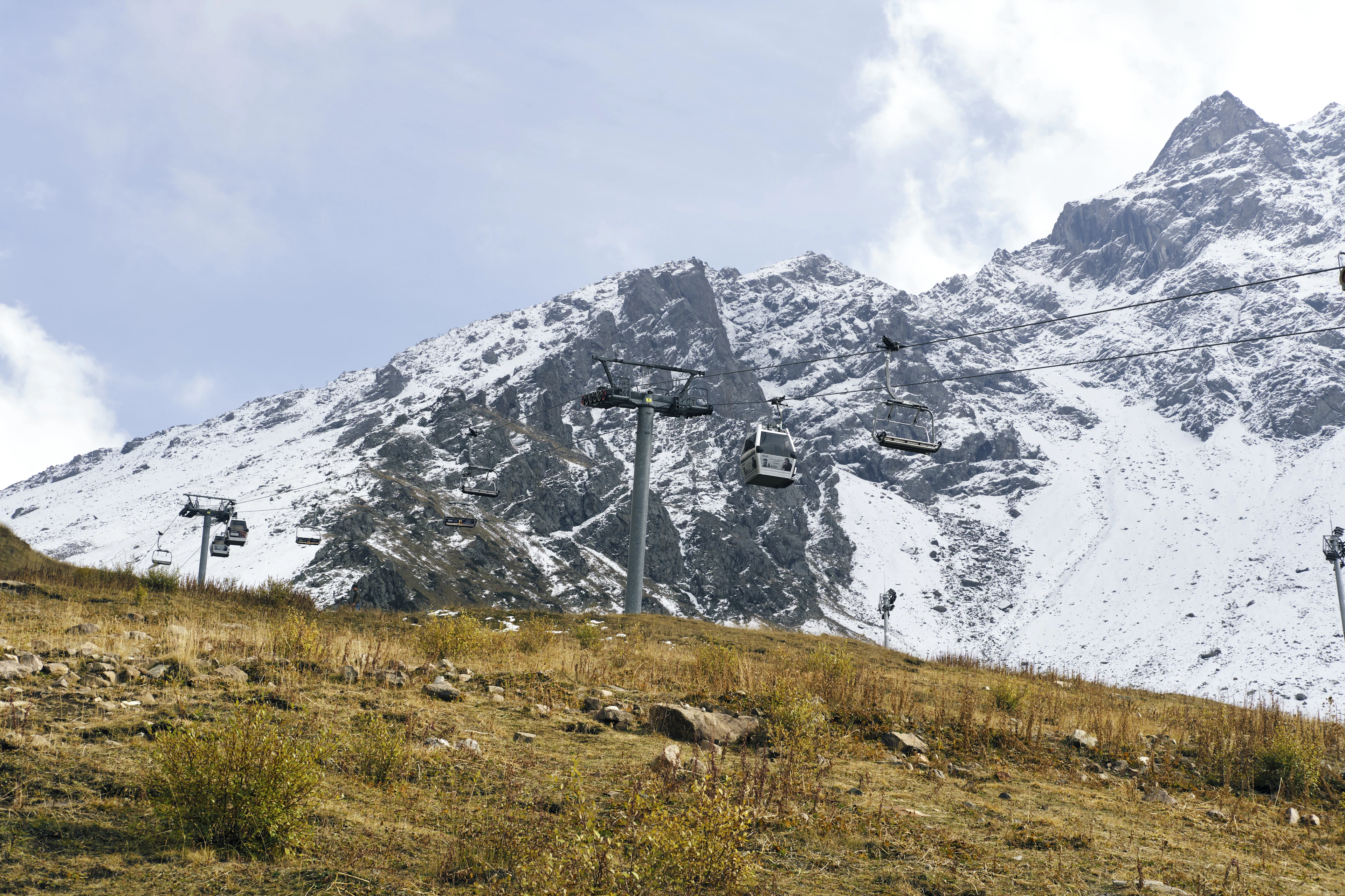 An empty chairlift climbs a steep, ridged snow-covered mountainside above Almaty under a pale sky.