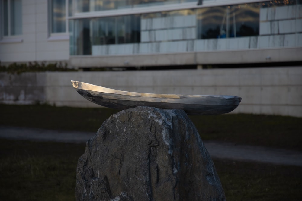 a metal object sitting on top of a rock in front of a building