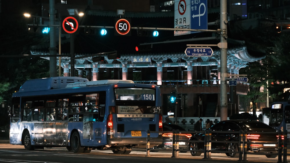 a blue bus driving down a street at night