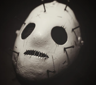 A twisted, rust-colored mask with jagged edges and haunting hollow eyes