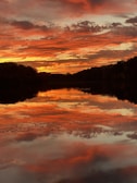 A vibrant sunset over a tranquil lake with reflections.