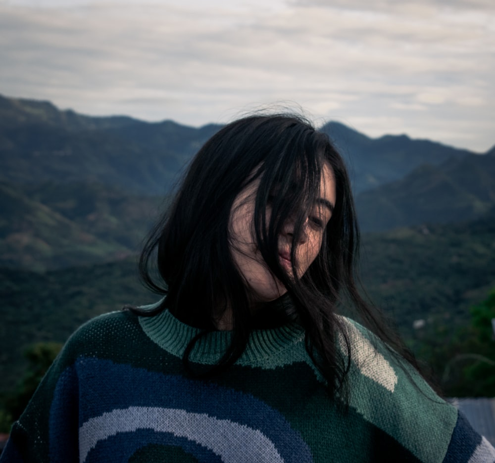 a woman with long hair standing in front of mountains