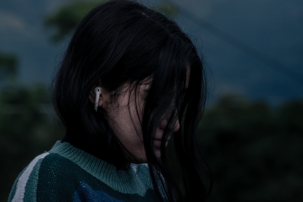 a woman with long black hair wearing a green and white sweater