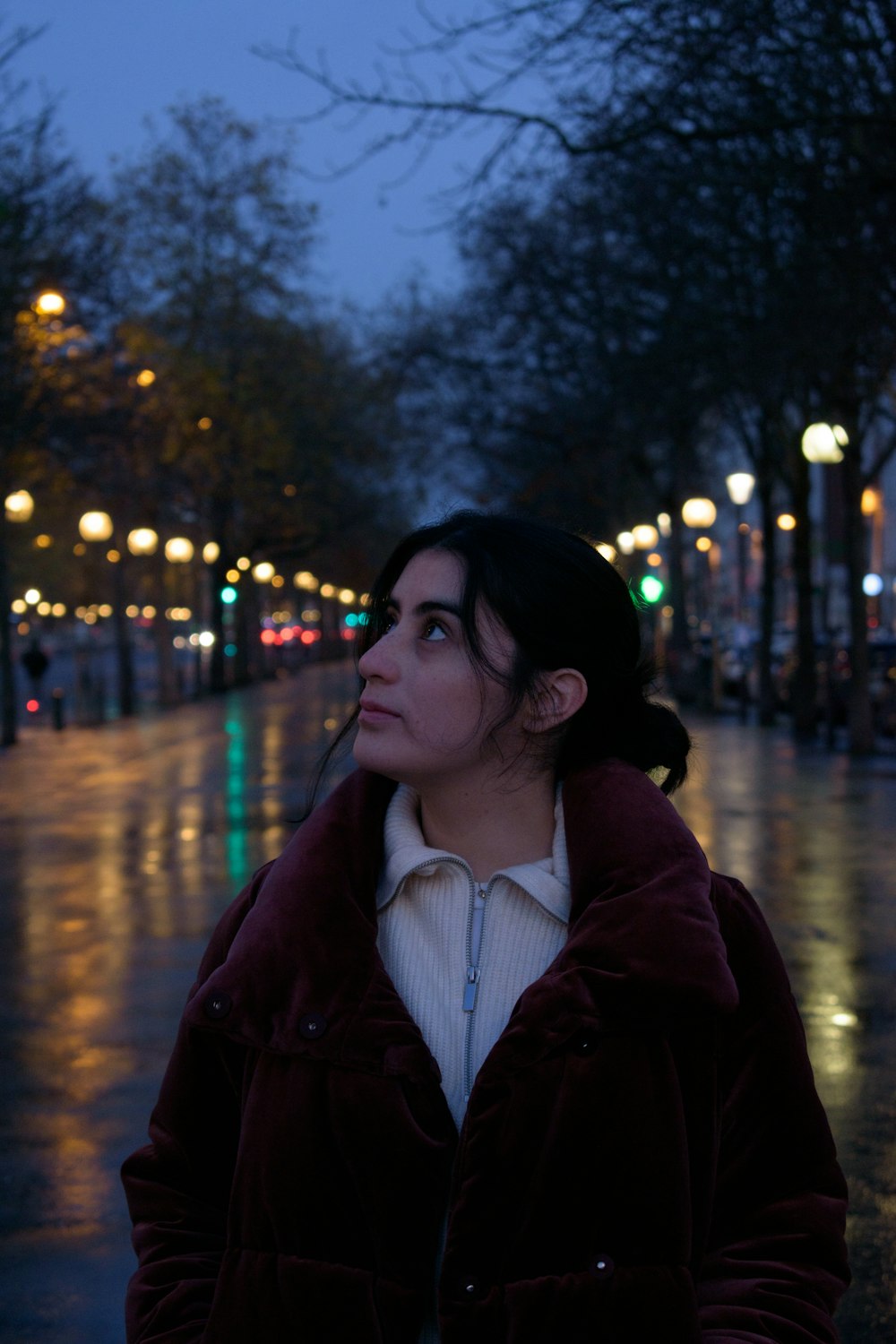 a woman standing on a wet sidewalk at night