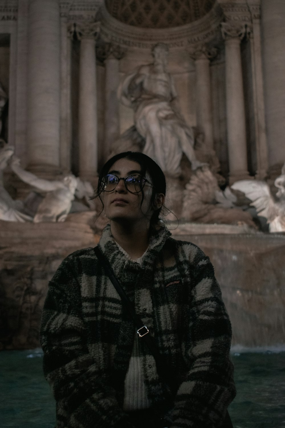 a man with glasses standing in front of a fountain