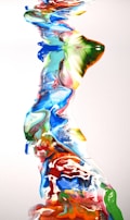 A dynamic flow of mixed colors creates a river-like pattern on a white background. The colors blend smoothly and include bright shades of blue, green, red, yellow, and orange, producing a vibrant and abstract appearance.