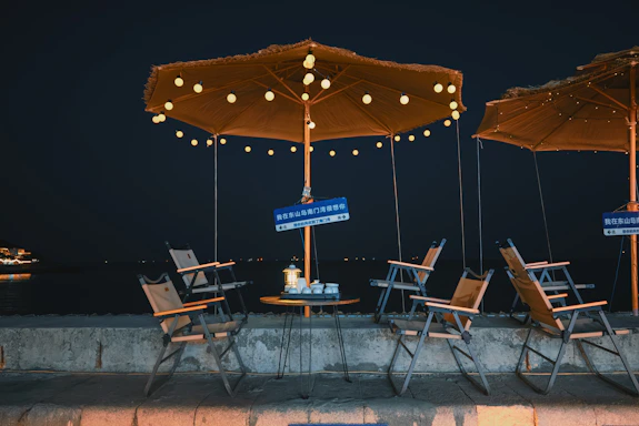 A cozy event setup featuring elegant chairs and tables arranged outdoors under string lights at dusk.