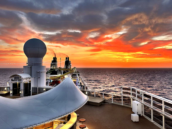 A vibrant Mediterranean cruise ship deck with wine glasses and sunset in the background.