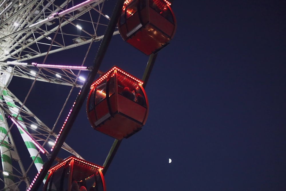 a ferris wheel lit up at night with the moon in the background
