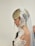 A bride is wearing a white lace veil and an elegant wedding dress. Her hair is styled in an updo with a loose strand flowing down, adding a romantic touch. The intricate lace detail of the veil frames her face delicately.