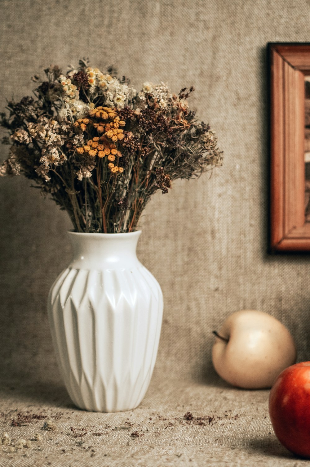 a white vase filled with dried flowers next to an apple