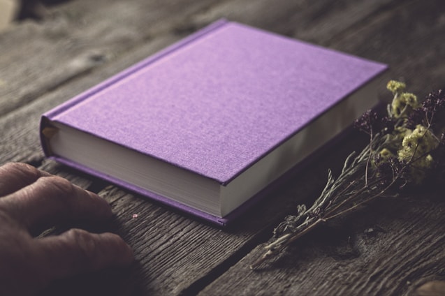 A close-up of a vibrant purple book cover with gold embossed lettering, resting on a clean, structured wooden desk.