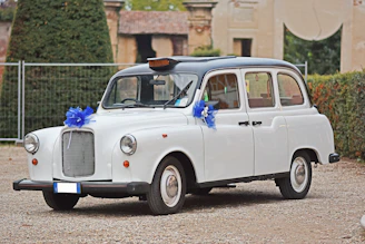 A modern black electric taxi parked outside a charming wedding venue with floral decorations.