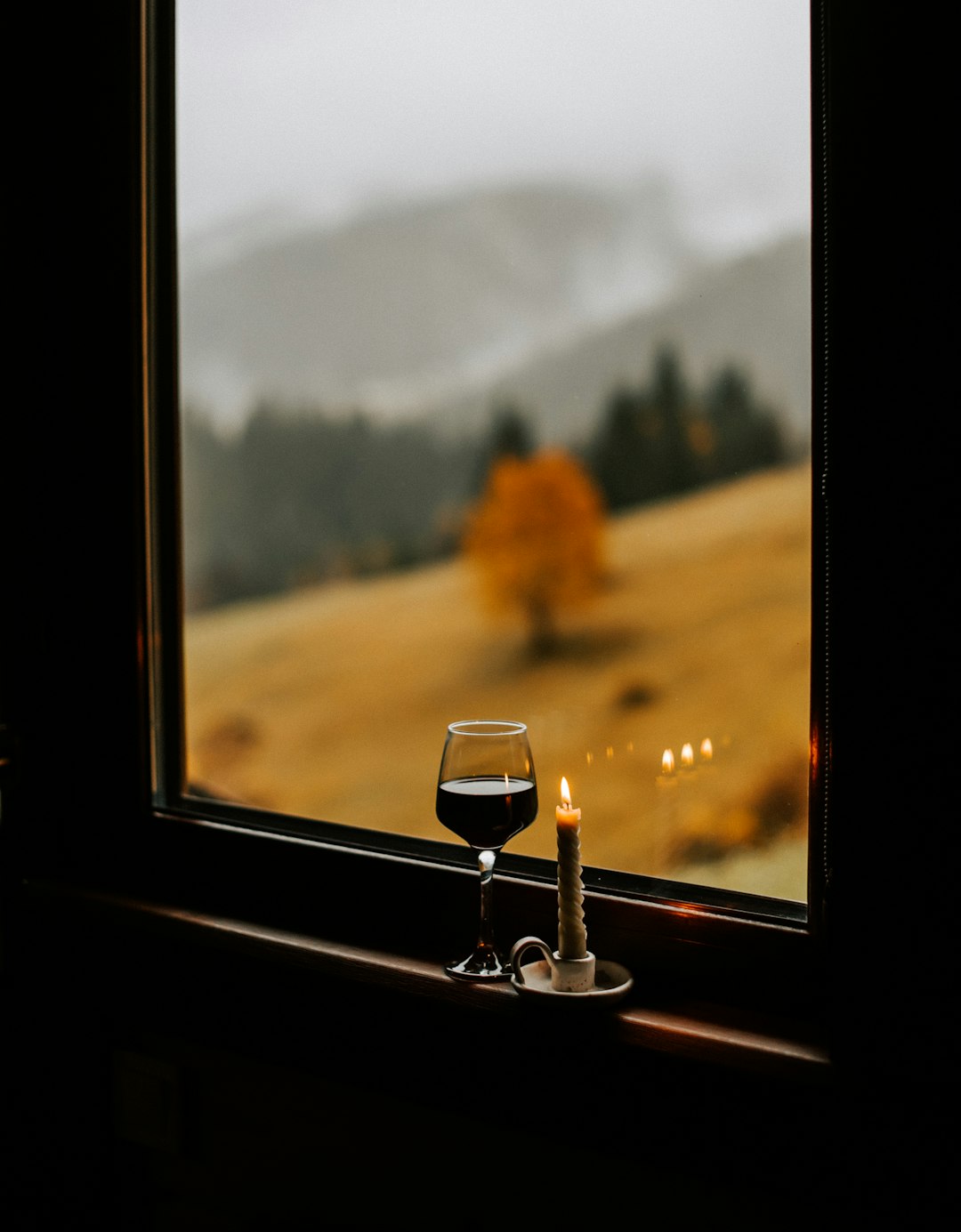 a candle and a glass of wine on a window sill