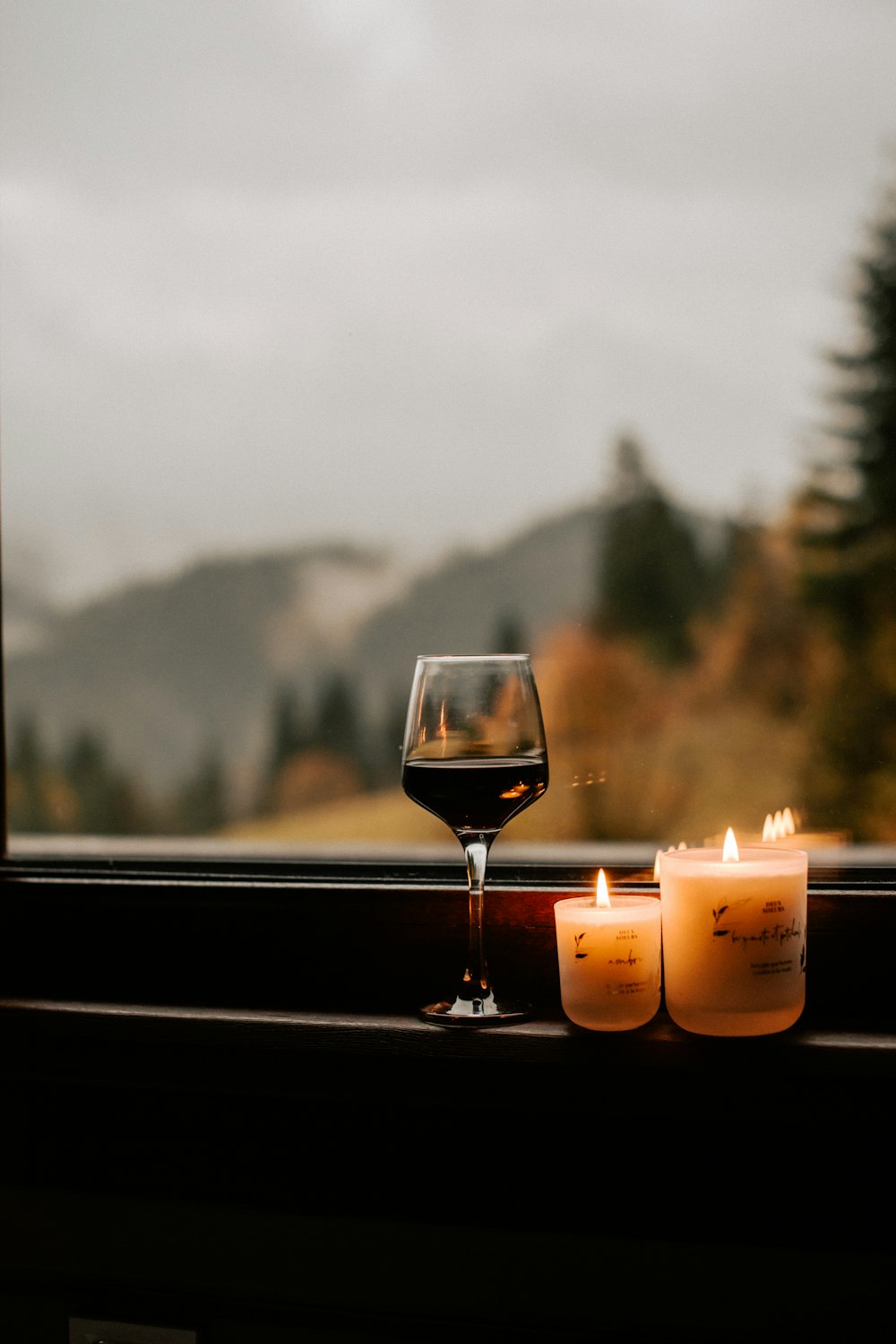 a glass of wine sitting next to two candles on a window sill