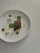 A close-up of a beautifully plated minimalist dish with fresh ingredients on a white ceramic plate.