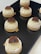 Several round pastries are arranged on a black serving tray. Each pastry has a light cream filling topped with a decorative brown chocolate piece. The surface of the pastries is smooth and creamy, with a slightly darker crust at the bottom.