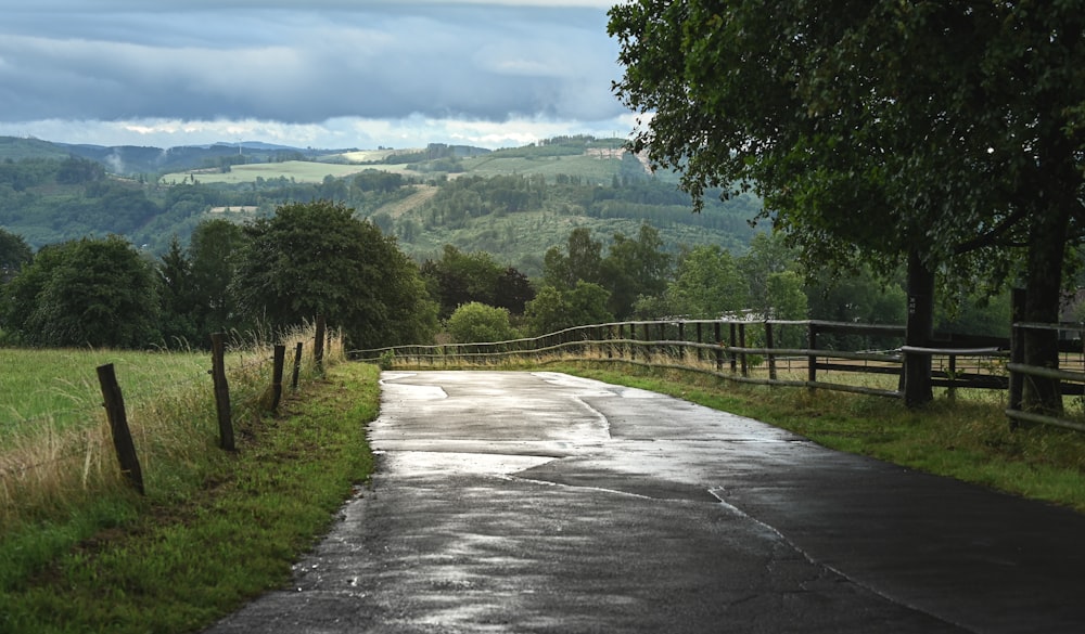 a wet road with a fence and a field in the background