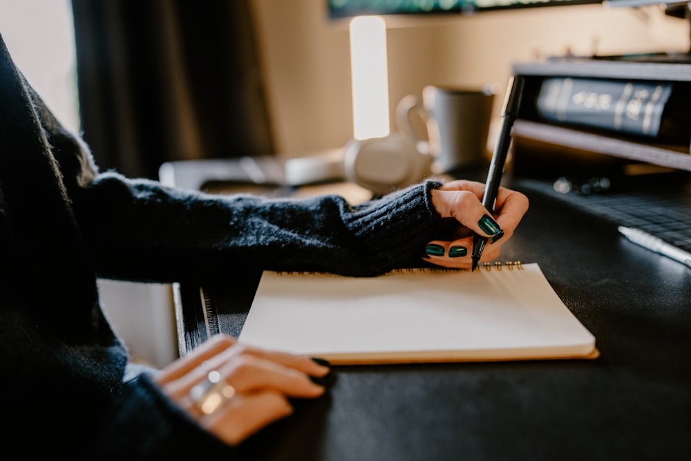 uma pessoa segurando uma caneta e escrevendo em um caderno