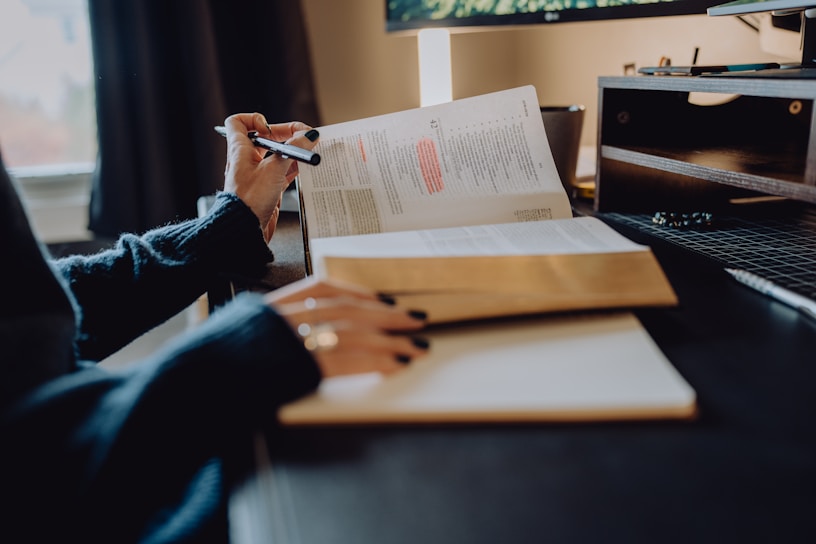 A thoughtful person writing notes while reading a book in a cozy study.