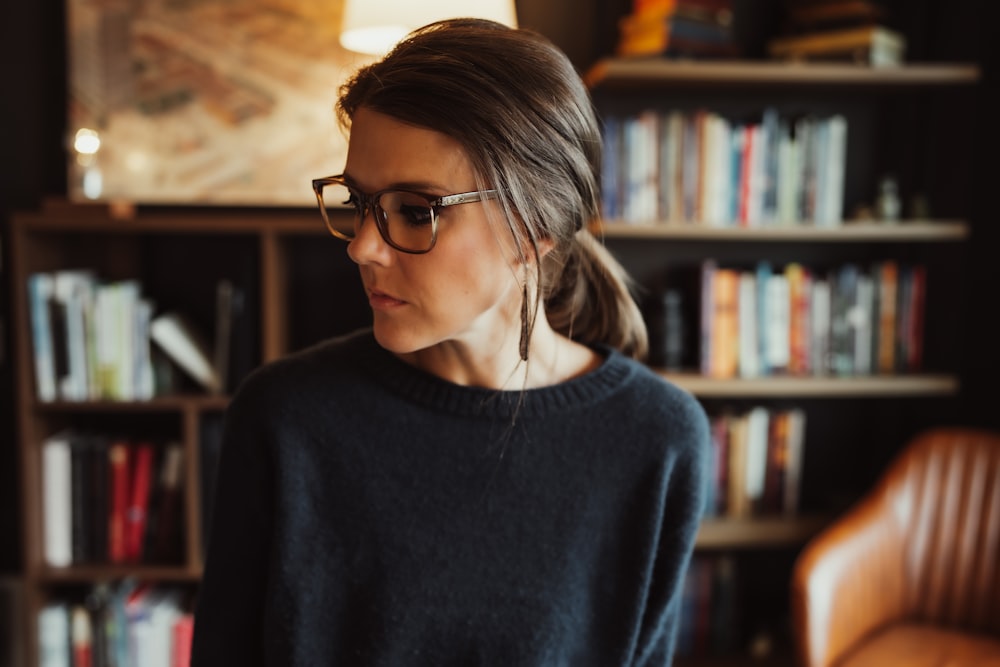 a woman wearing glasses standing in front of a bookshelf