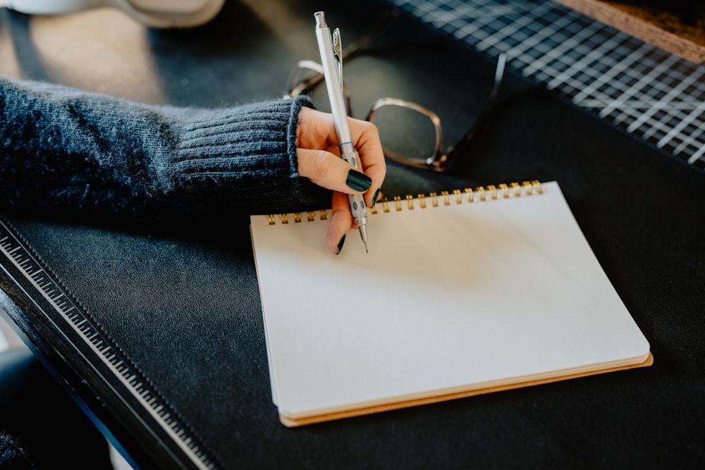 a person holding a pen and writing on a notebook