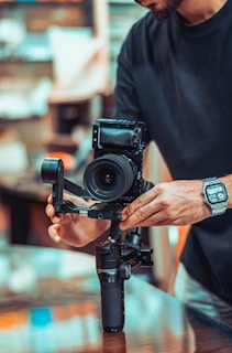 A person adjusts a professional camera mounted on a stabilizer, with focus on technical equipment in a setting that appears to be a studio or workspace. The scene conveys a sense of precision and craftsmanship.