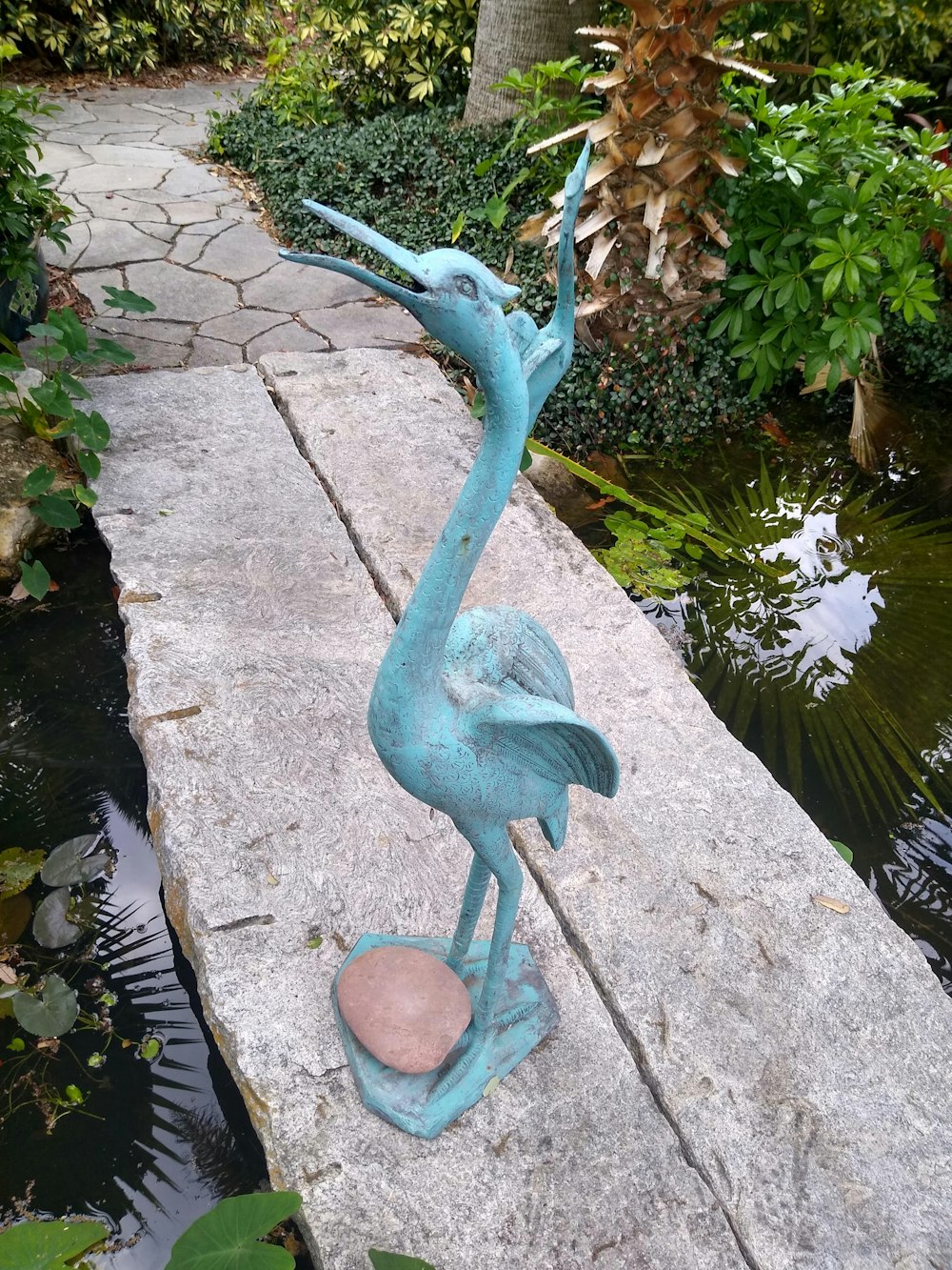 a statue of a bird on a rock near a pond