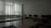 A dimly lit classroom or computer lab with several empty desks and a row of computer monitors along one wall. The window has closed vertical blinds, allowing minimal light to filter through.