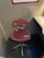 A chair with a red cushioned seat and backrest, labeled with 'TGV' and 'SNCF' logos, is positioned in a small, enclosed space near a desk. The chair has a metal base with a swivel feature. Above the chair, a framed schedule or chart is mounted on the wall.